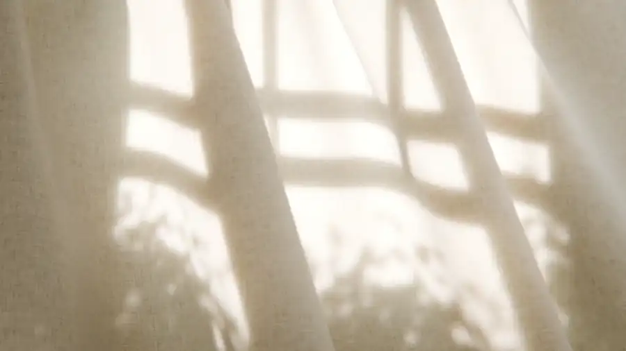A patterned curtain lifting in the wind with sunlight behind it